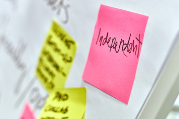 Word independent written on pink and yellow paper stickers attached to a flip chart on a whiteboard