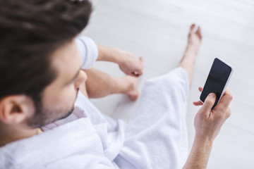 Obraz na płótnie Canvas selective focus of bearded man in bathrobe using smartphone with blank screen