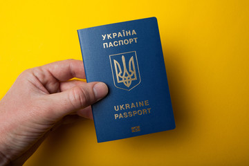 Biometric Ukrainian passport in hand on a yellow background.