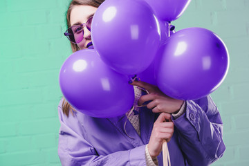 young woman in sunglasses hiding behind purple balloons