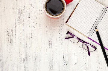 Pencil, notebook, glasses and a cup of coffee on a white wooden table.