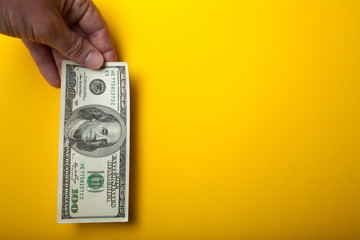 A hundred dollars in hand on a yellow background, empty space for text.