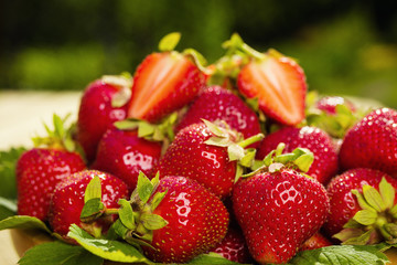 strawberries in basket on wooden table in natural background, delicious first class organic fruit as a concept of summer vitamins