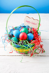 Image of basket with colorful eggs on empty blue background on wooden table