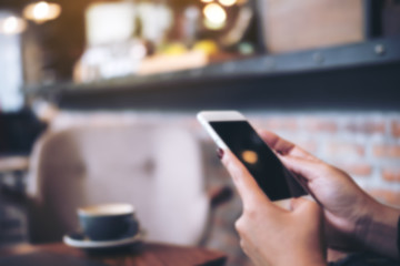 Blur image of a woman holding and using smart phone in modern cafe