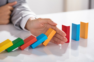 Businessperson Hand Stopping Colorful Blocks From Falling