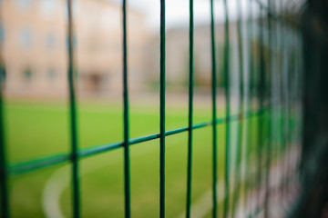 Close up metallic net-shaped green fence on a background of football field