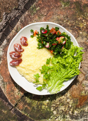 Millet porridge with fresh green salad leaves, sausage and vegetables.