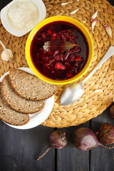 Red traditional russian and Ucrainian borscht or beetroot soup with sour cream, garlic and flavorings in a yellow ceramic cup on wicker placemat background.