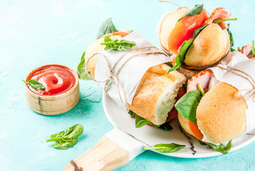 Fresh baguette sandwich with bacon, cheese, tomatoes and spinach, light blue background copy space