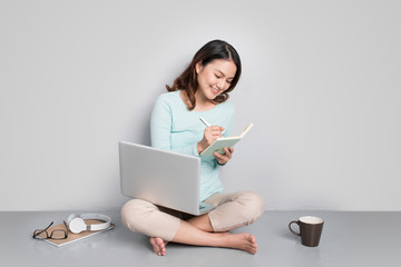 Happy casual beautiful asian woman working on a laptop sitting on floor at home.