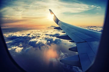 Fototapeten Fliegen und Reisen, Blick aus dem Flugzeugfenster auf dem Flügel bei Sonnenuntergang © babaroga