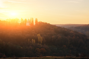 Fototapeta premium Landscape of old solitary church on the hill with autumn forest during the sunset