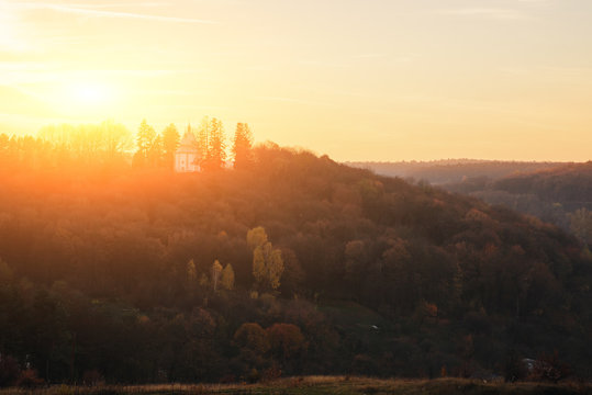 Fototapeta Landscape of old solitary church on the hill with autumn forest during the sunset