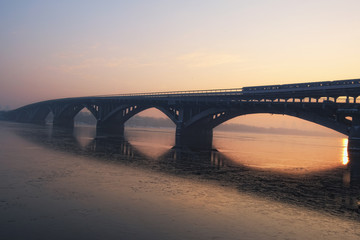 Merto (subway) Bridge at winter sunrise, viewed from embankment of the Dnieper River. Kyiv, Ukraine