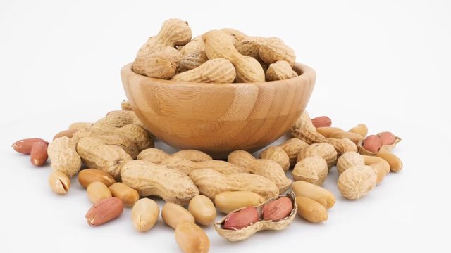 Peeled and whole peanuts in wooden bowl in rotation isolated on white