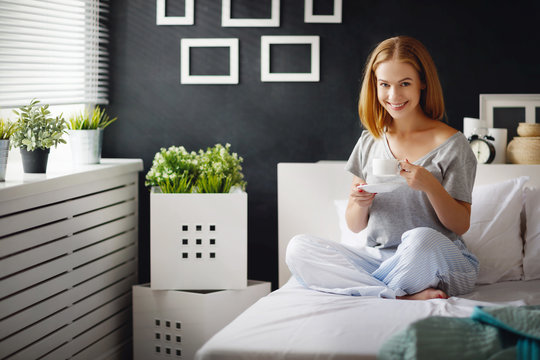 happy young woman with cup of morning coffee in bed