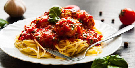 pasta spaghetti with meatballs in tomato sauce on a plate on dark wooden background