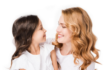 Obraz na płótnie Canvas portrait of smiling daughter and mother looking at each other isolated on white