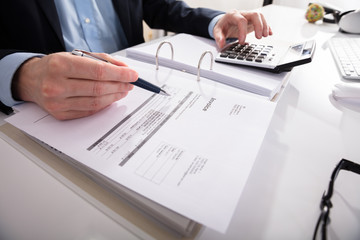 Businessperson Checking Invoice With Calculator
