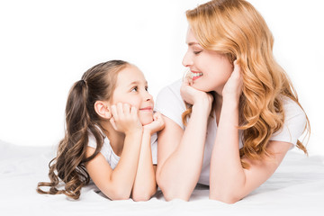 Obraz na płótnie Canvas portrait of smiling mother and daughter looking at each other isolated on white