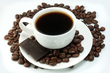 White cup of coffee with a bunch of coffee beans and pieces of chocolate on a white background
