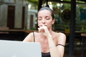 Fototapeta premium Meditating female copywriter works remotely, using modern notebook, enjoys tasty beverage, uses good internet connection. Woman in coffee shop trying concentrate, closing eyes, researching new ideas.
