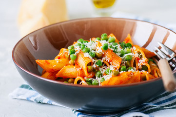 Tomato sauce and green peas penne pasta in a plate on a white stone background