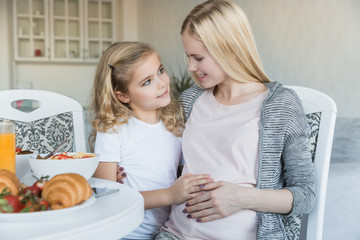 daughter touching pregnant mother belly in kitchen