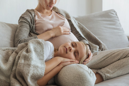 cropped image of daughter sleeping on pregnant mother legs