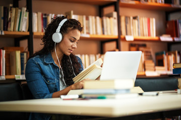 Young female student with curly hair study in the school library.She using laptop and learning online.