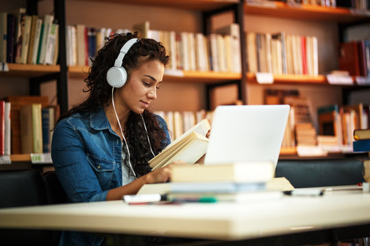 Young Female Student With Curly Hair Study In The School Library.She Using Laptop And Learning Online.