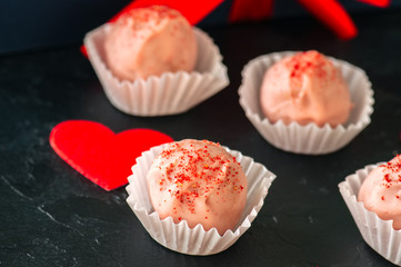 White chocolate and strawberry truffles on black stone background