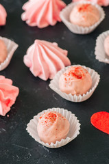 White chocolate strawberry truffles and pink meringue kisses on black stone background