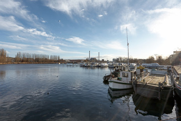 Fototapeta premium Pier with Boats on a Branch of River, under a Blue Cloudy Sky, with Industry Buildings