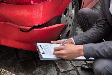 Insurance Agent Writing On Clipboard After Car Accident