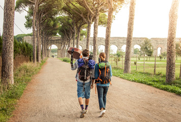 Obraz premium Young couple backpackers tourists with guitar walking towards roman aqueduct ruins in acquedotti park in rome.