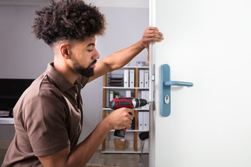 Fototapeta na wymiar Carpenter Installing Door Lock With Wireless Screwdriver