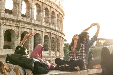 Three young friends tourists sitting lying in front of colosseum in rome taking selfie pictures...