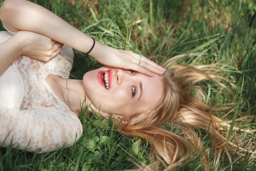 Outdoor portrait of beautiful blonde girl lying on green grass