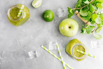 Green healty drink in mason jar with green apple, mint, lime and melting ice cubes on grey background. Vegetarian food concept. Detox. Text space