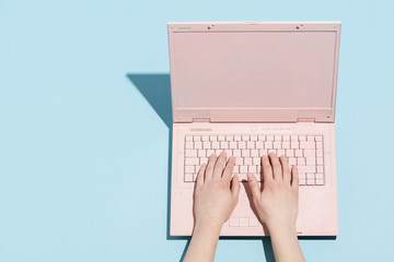 Woman's hands typing on a pastel pink keyboard