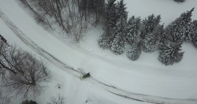Aerial shot of a man using a tractor to clear snow from a driveway.  Snowy, winter day in Canada.  Drone shot. 4K.