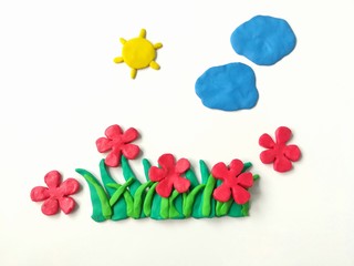 Colorful plasticine clay dough made are red flowers grass sun and clouds on white background, beautiful nature