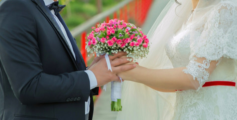 They held the pink flower bouquet in their hands . hands folded behind their back, hold a beautiful little wedding bouquet of roses . 