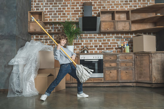 adorable happy little boy playing with mop in new house