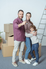 happy family with one kid smiling at camera and holding key from new apartment