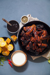 Chicken wings in thick barbecue sauce with garlic on black cast iron pan on gray rustic background.