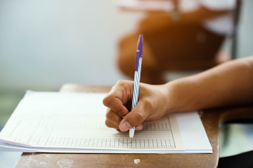 Closeup to hand of student  holding pen and taking exam in classroom with stress for education test.