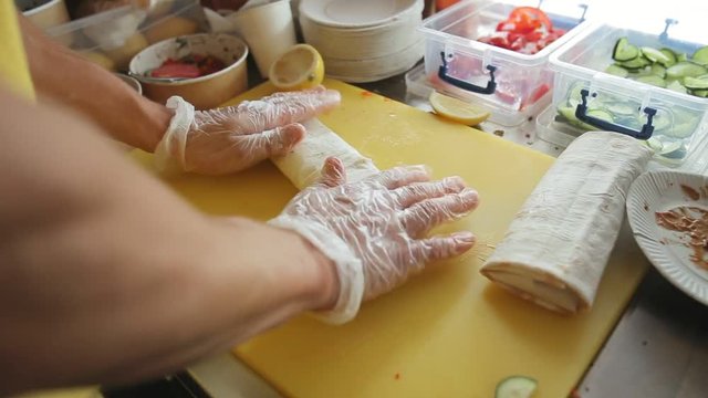 Cook's hands in disposable gloves wrap up doner kebab